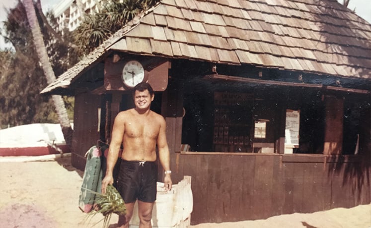 Leleo Kinimaka, master woodworker, stands in front of a building